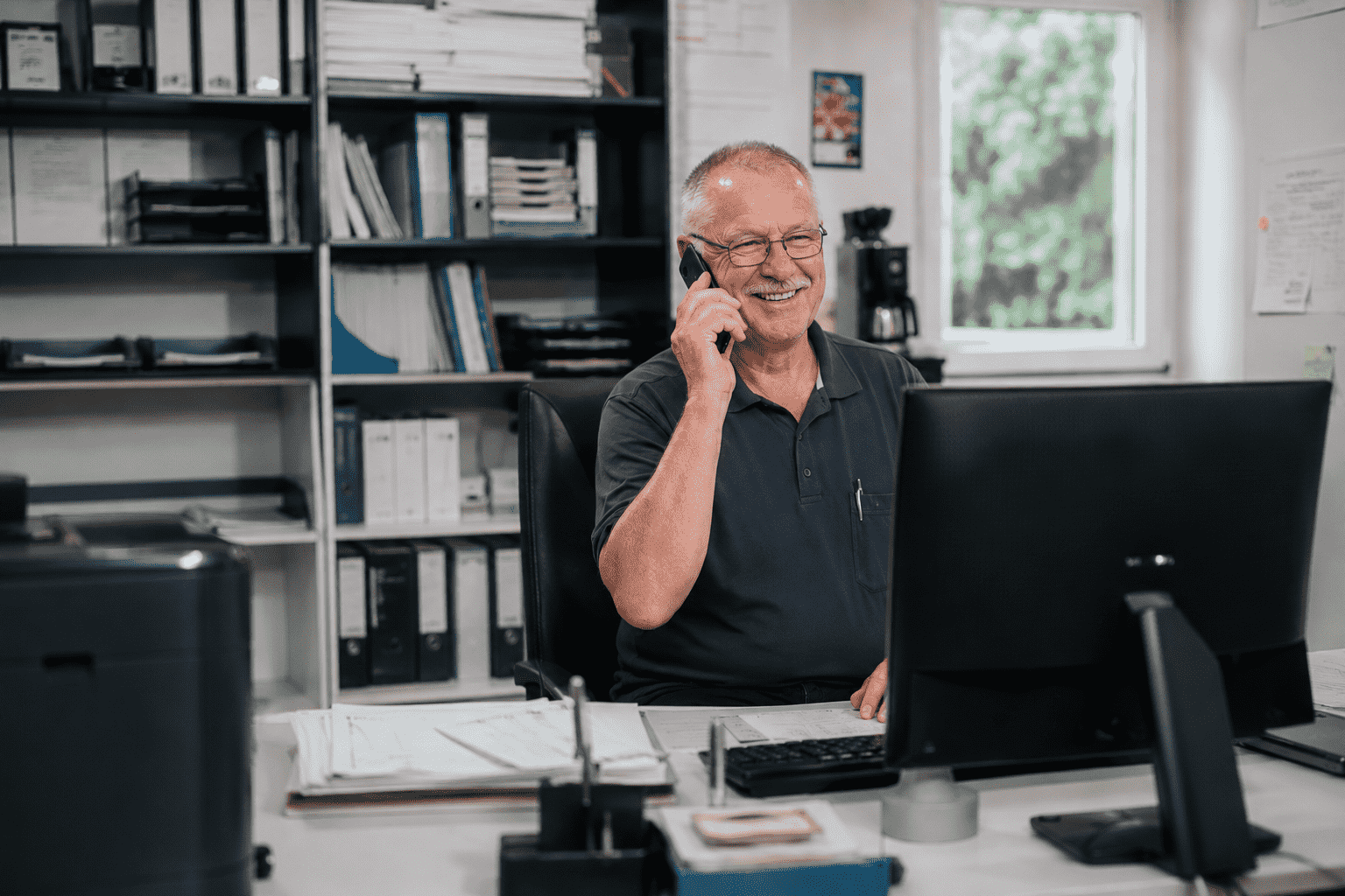 Älterer Mann telefoniert lächelnd am Schreibtisch im Büro