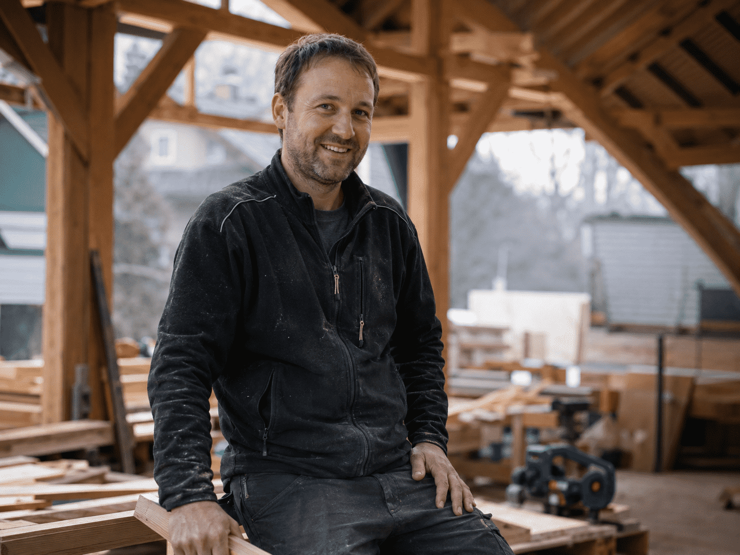 Lächelnder Handwerker in einer Holzwerkstatt sitzt auf einem Balken