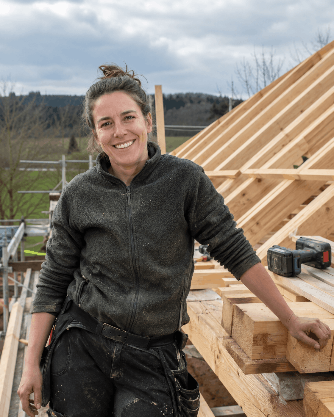Eine lächelnde Frau auf einer Baustelle mit Holzgerüst und Werkzeugen