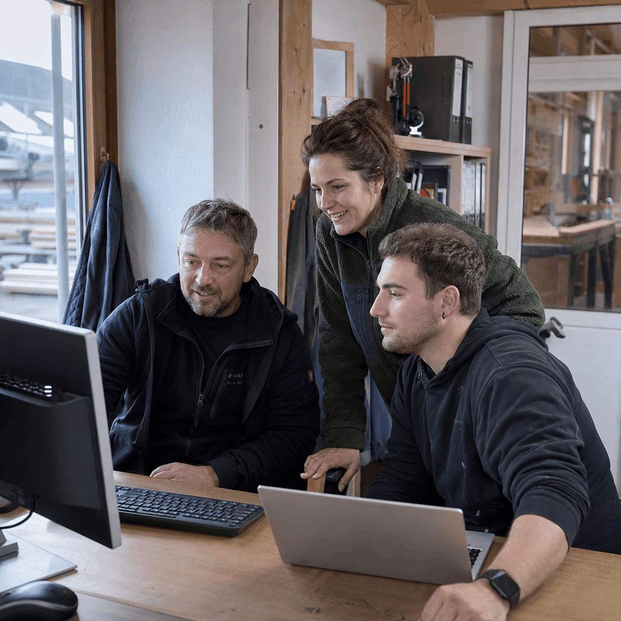 Drei Personen arbeiten gemeinsam an einem Computer im Büro